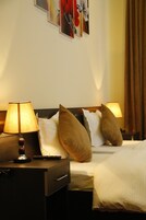 Habitación de hotel con cama, dos lámparas de noche, una mesita de noche y un cuadro floral en la pared.