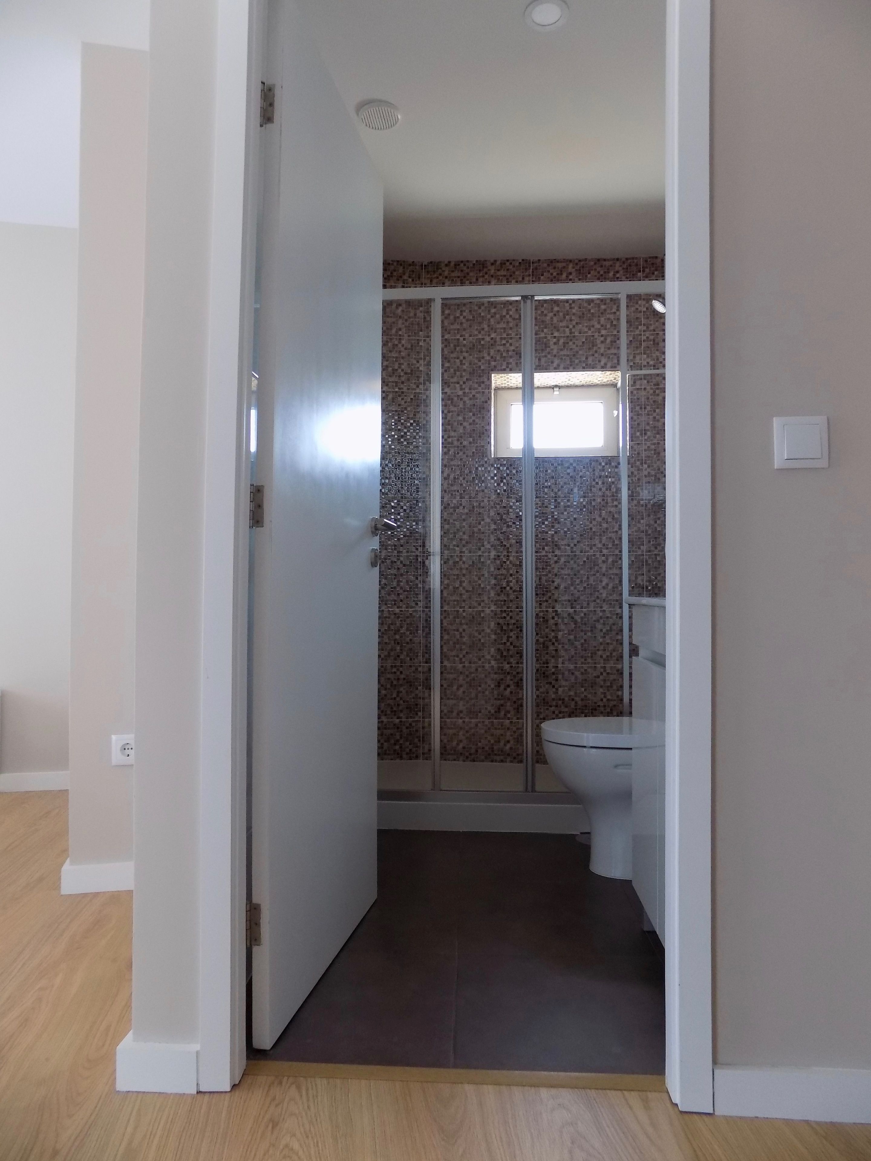 A bathroom with a shower, toilet, and a small window.