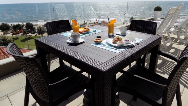 Una mesa preparada para el desayuno con vistas al mar, sillas de mimbre y cielo despejado.