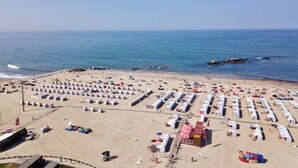 Una playa con filas de tiendas de campaña blancas y sillas de playa, una torre de salvavidas y una vista despejada del océano.