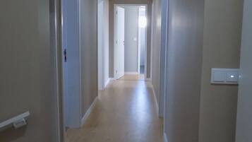 A narrow, well-lit hallway with wooden flooring and white walls.
