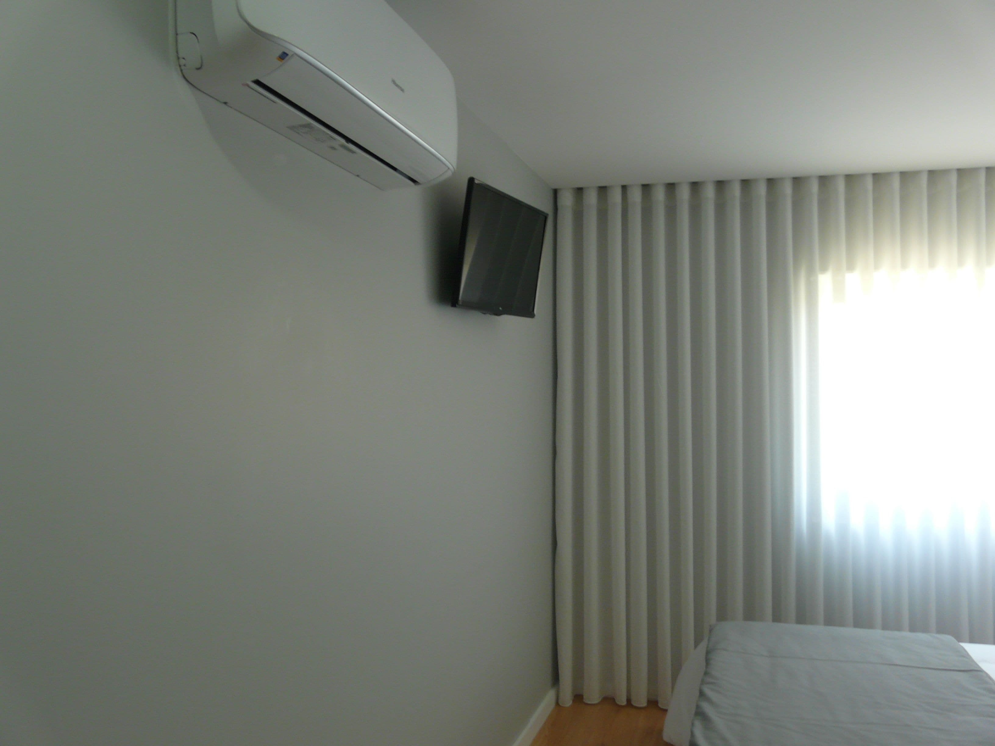 Un dormitorio con cama, aire acondicionado y televisor montado en la pared.