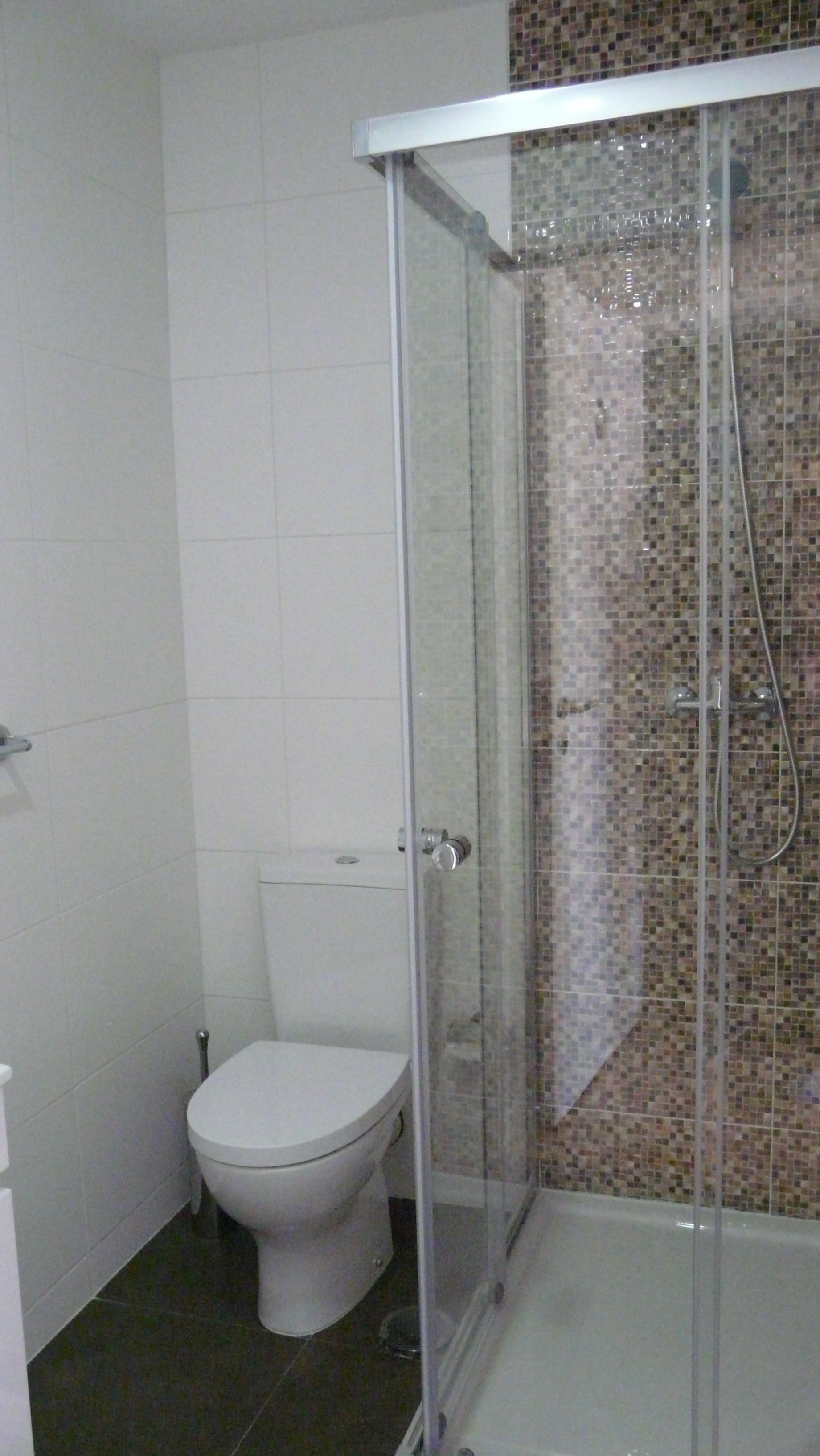 A bathroom with a toilet, a glass-enclosed shower, and tiled walls.