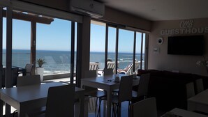 Un comedor moderno con grandes ventanales con vistas al océano, un televisor de pantalla plana en la pared y un letrero que dice 'GUESTHOUSE'.