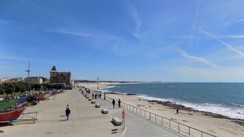 A coastal promenade with a stone pathway, beach, and a historic building.