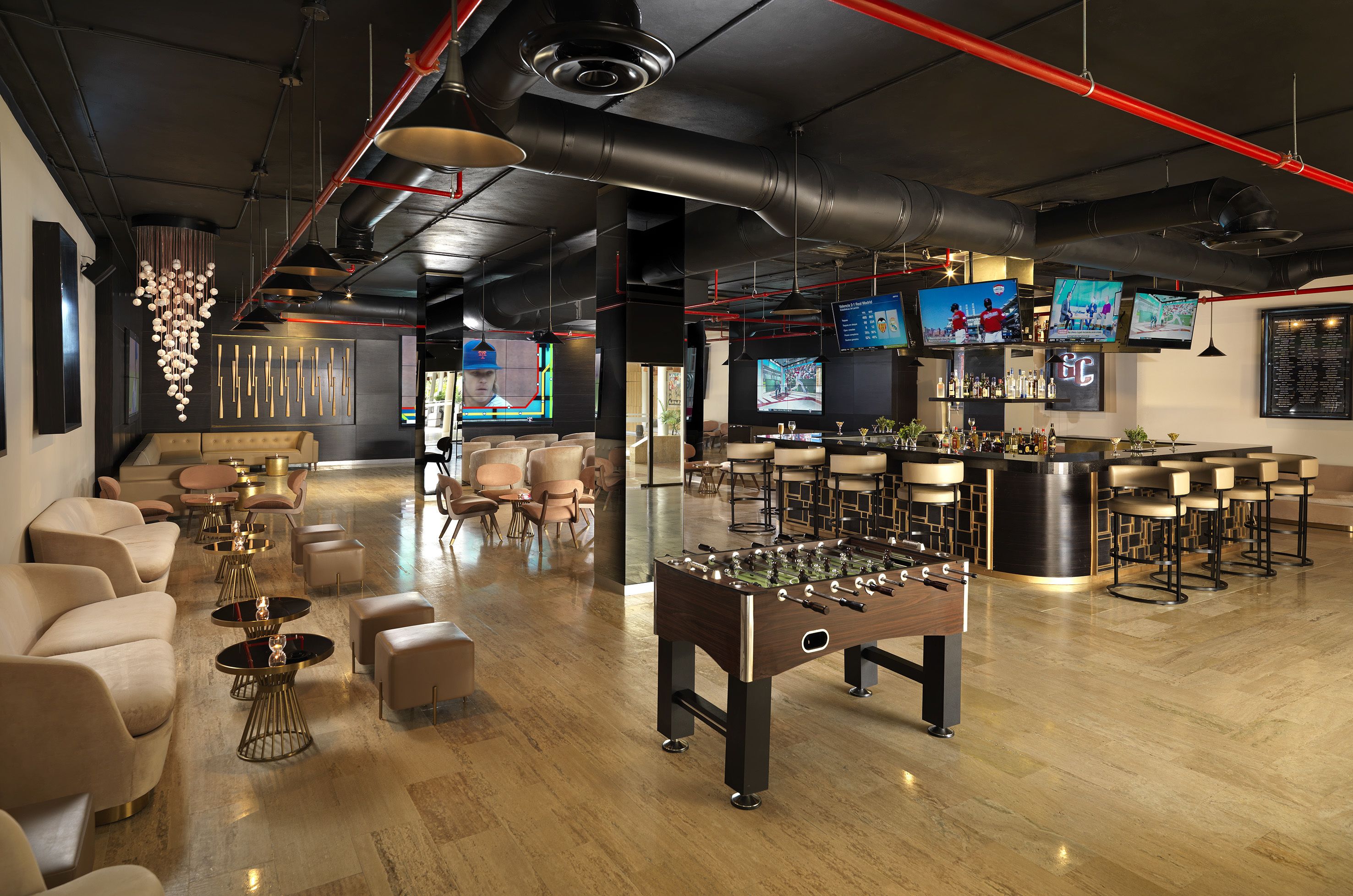 A modern bar area with a foosball table, multiple TVs, bar stools, and a seating area with sofas and tables.