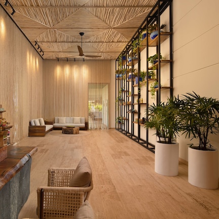 A spacious lobby with a wooden reception desk, a seating area with sofas, and a wall with shelves holding plants.