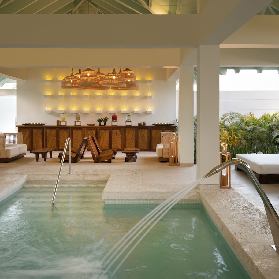 A pool area with a lounge, wooden furniture, and a bar with ambient lighting.