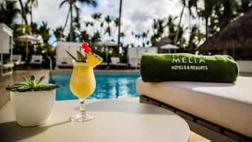 Une scène de bord de piscine avec une boisson, une plante en pot et une serviette arborant le logo « MELIA HOTELS & RESORTS ».