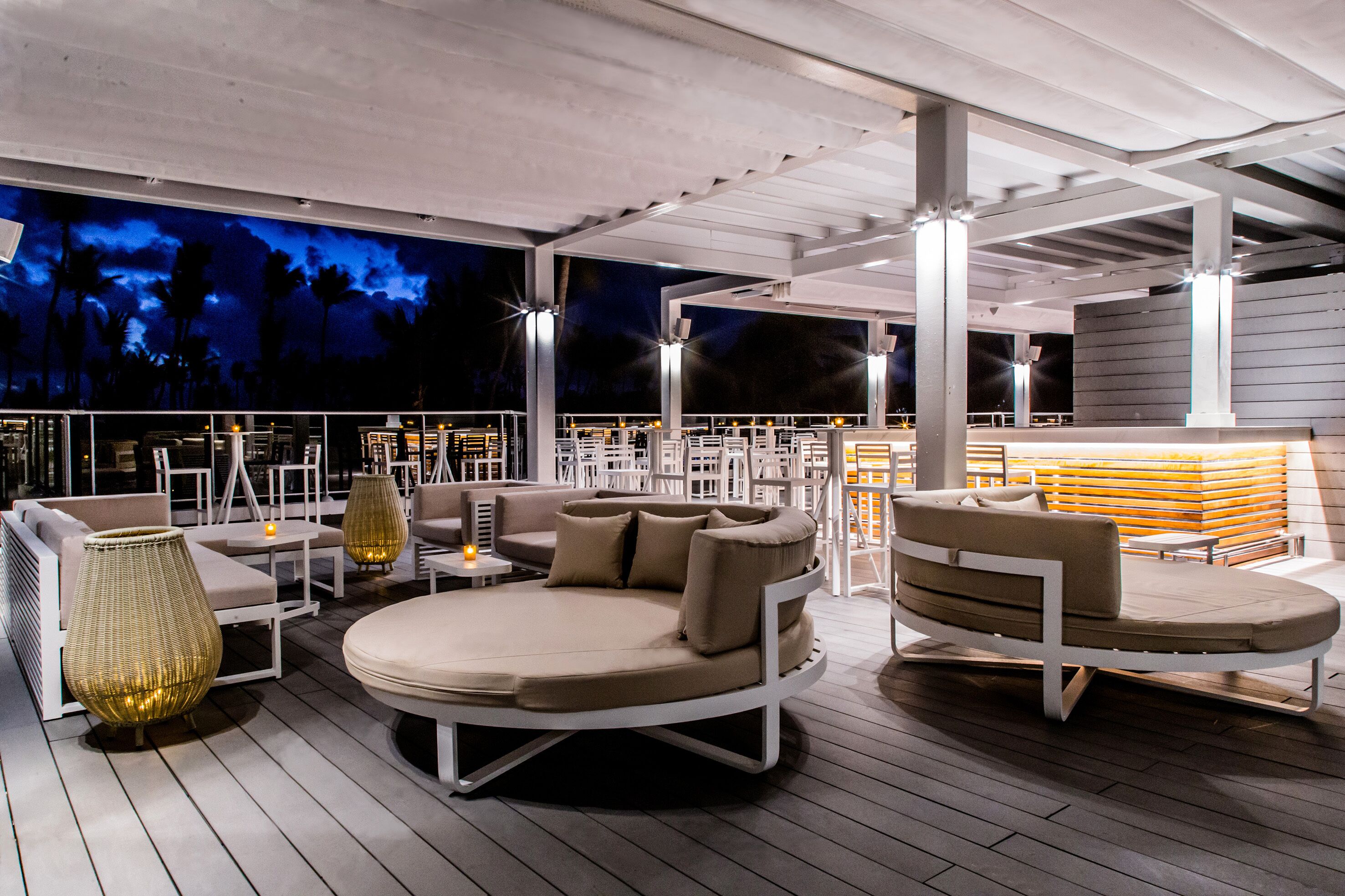 Un área de lounge en la azotea con asientos redondos, mesas y vistas al cielo nocturno.