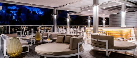 Un área de lounge en la azotea con asientos redondos, mesas y vistas al cielo nocturno.