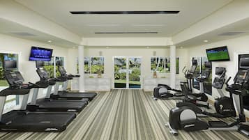 Un gimnasio con cintas de correr, elípticas y bicicletas estáticas, con amplias ventanas y vistas a zonas verdes.