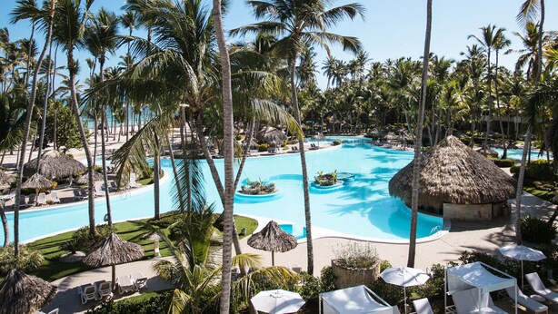 Un complexe hôtelier doté d’une grande piscine, entourée de palmiers et de chaises longues.