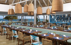 Enjoy a meal with a view of the ocean from our restaurant, featuring tables and chairs under a thatched roof.