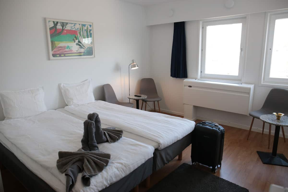 Hotellihuone, jossa on sänky, työpöytä, tuoli, lamppu, ikkuna ja matkalaukku.