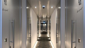 A hotel hallway with a patterned carpet, mirrored doors, and a ceiling with recessed lighting.