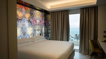 A hotel room with a large bed, a view of the sea, and a colorful wall mural.