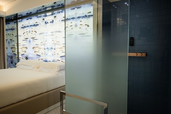 Una habitación de hotel moderna con una cama grande, un separador de vidrio y una pared con azulejos azules.