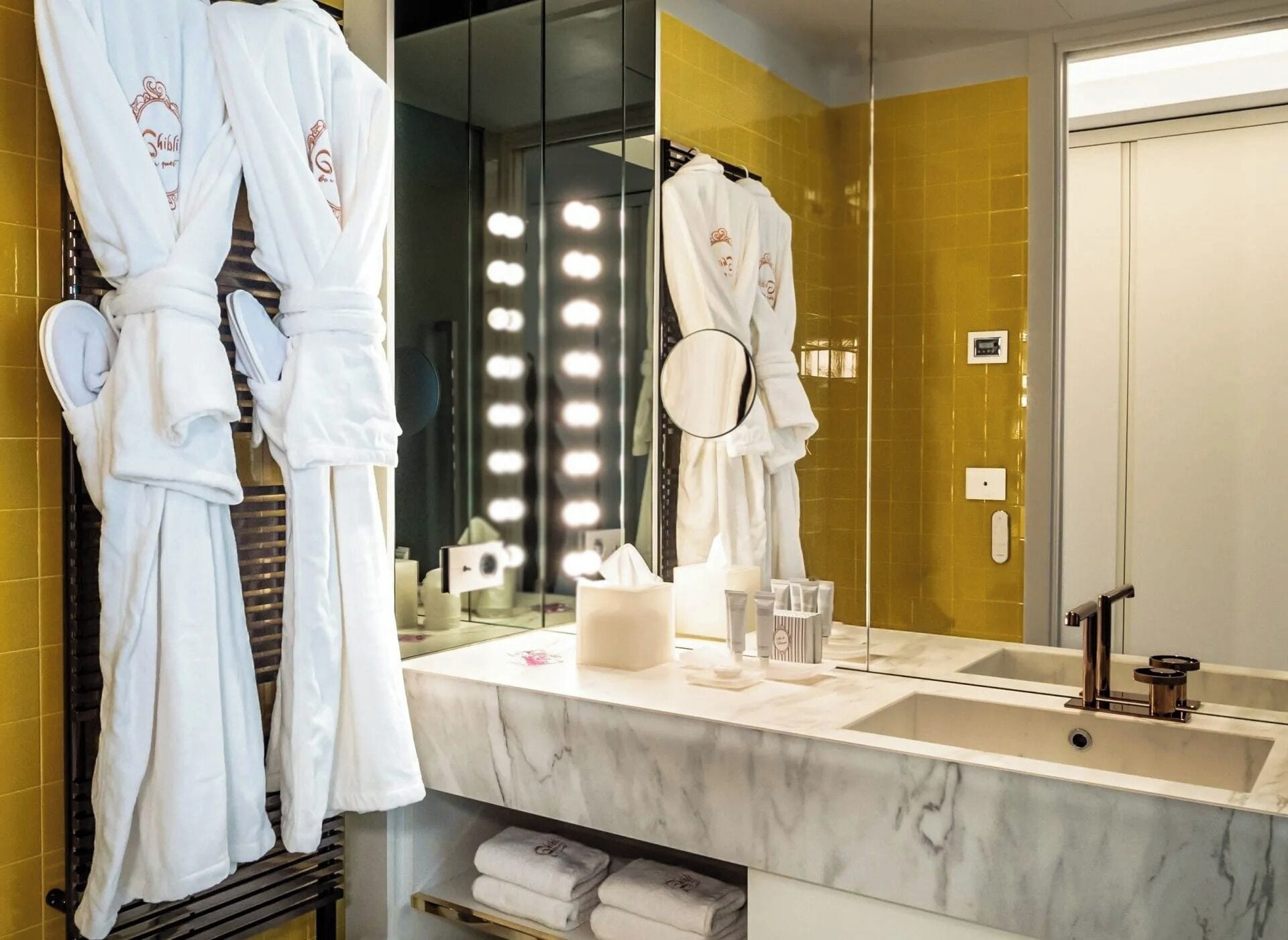 A bathroom with a large mirror, a sink, and two white robes hanging on a rack.