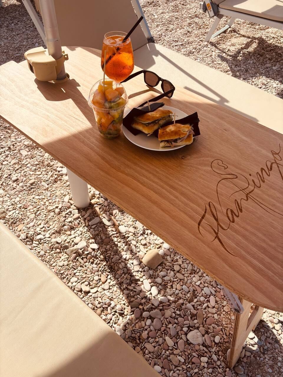 A wooden table with a plate of sandwiches and a drink, and a bench with a name engraved on it.