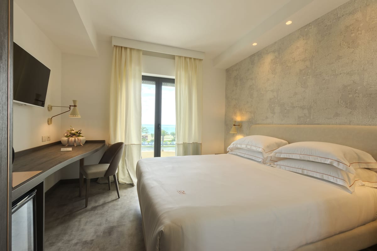 A hotel room with a bed, a desk, a chair, a TV, and a view of the outdoors.