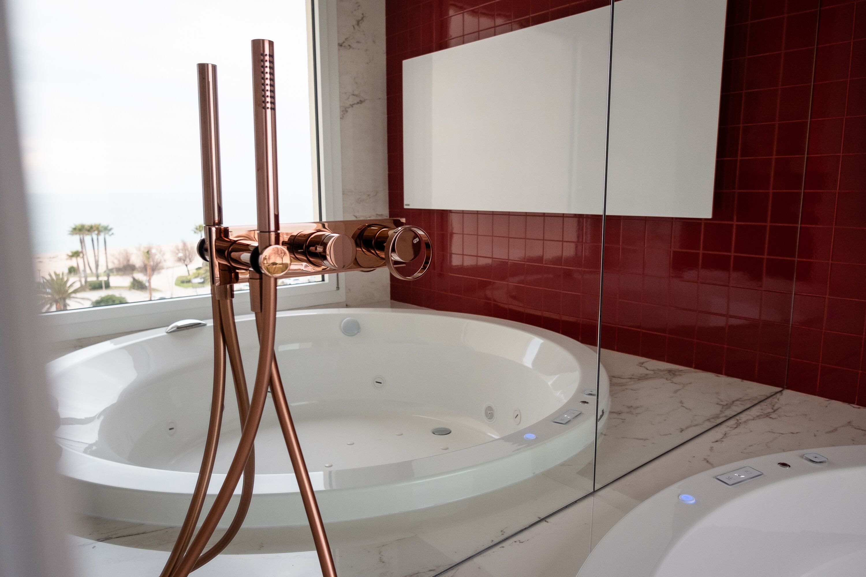A modern bathroom with a large bathtub, a glass-enclosed shower area, and a red-tiled wall.