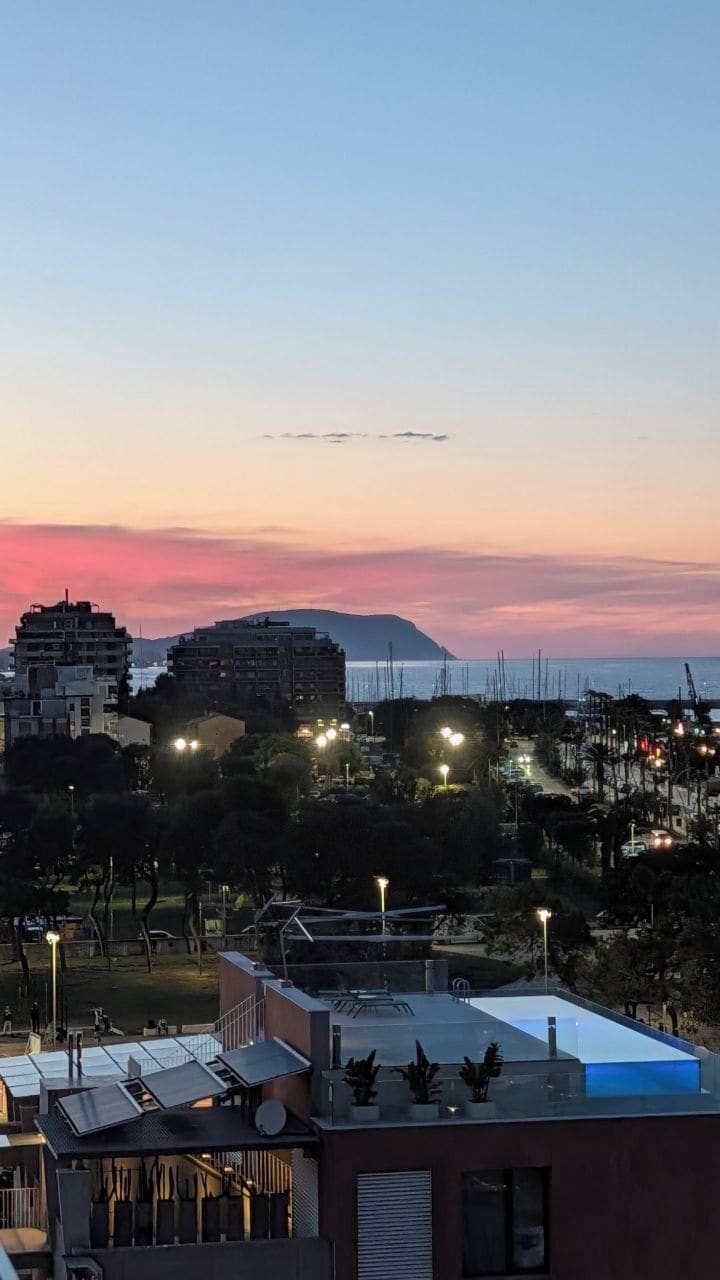 A coastal cityscape at dusk with buildings, street lights, and a clear sky.