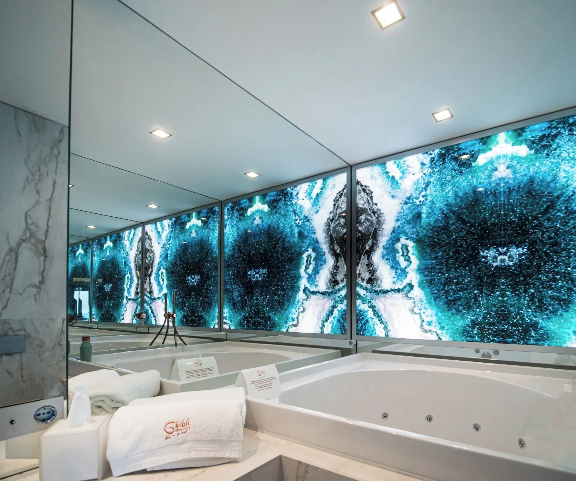 Un baño moderno con un espejo grande, una bañera y una pared con un diseño abstracto en azul.