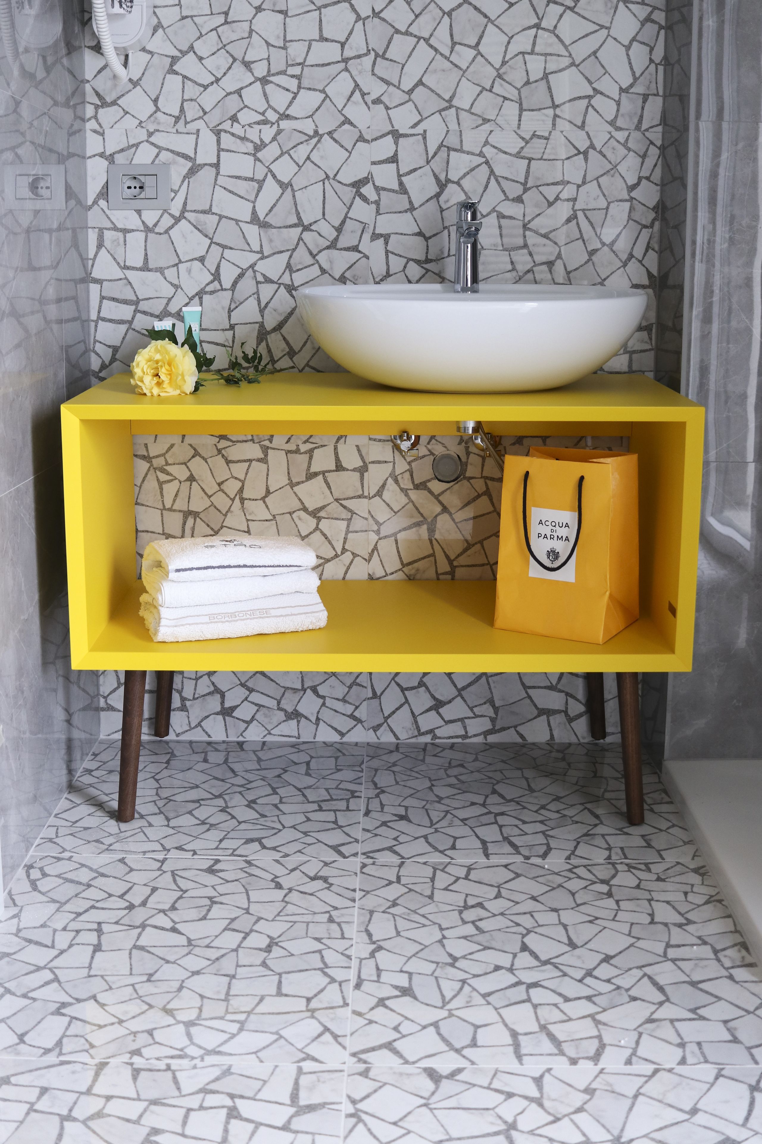 Un baño con tocador amarillo, lavamanos blanco y un salpicadero decorado.