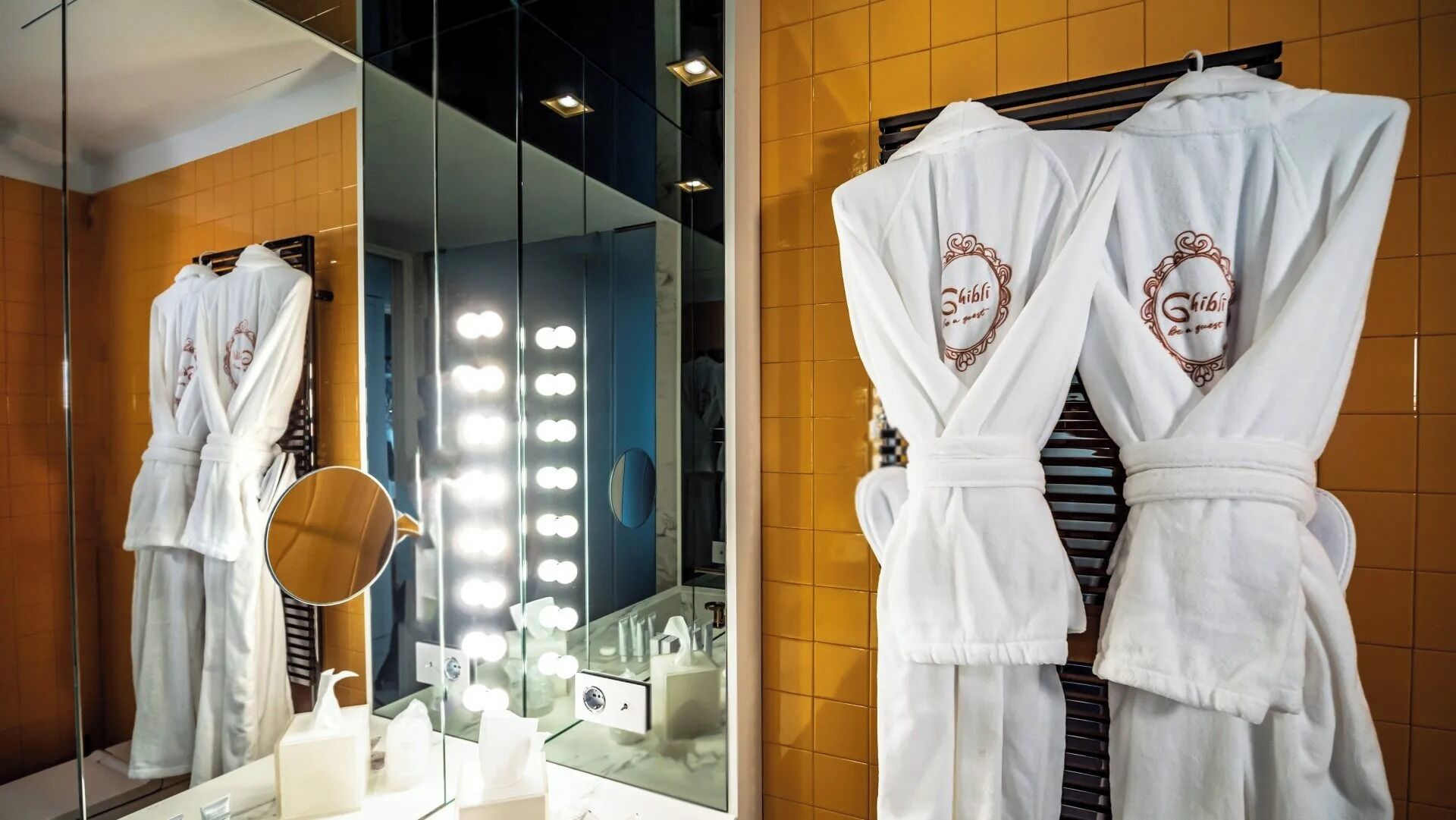 Une salle de bain d’hôtel avec un grand miroir, un meuble-lavabo et des crochets pour les peignoirs.
