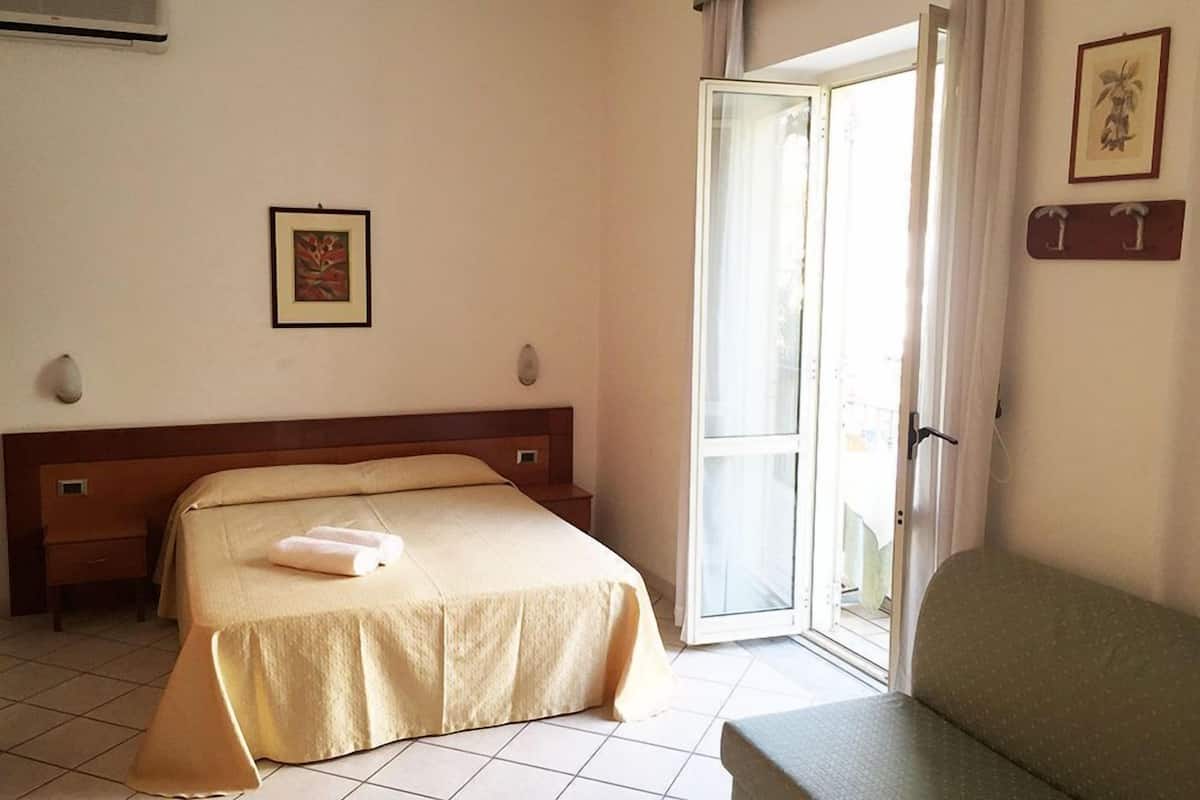 Une chambre d’hôtel avec un lit, une chaise, une fenêtre avec des rideaux et un climatiseur fixé au mur.