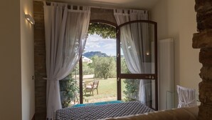 Un dormitorio con cama, ventana con cortinas, vista a un jardín y pared de ladrillo.