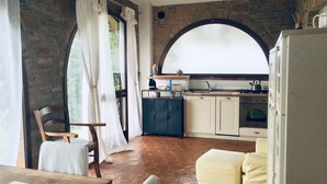 Una cocina rústica con un amplio ventanal de arco, un comedor con mesa y sillas de madera, y una zona de estar acogedora con cojines.