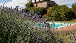 Un edificio de piedra con piscina y campos de lavanda al frente.