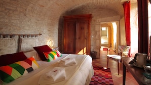 Een slaapkamer met een groot bed, een houten garderobe, een stoel en een tafel met een waterkoker.
