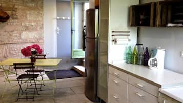 A compact kitchen with a dining area, featuring a stone wall, a refrigerator, cabinets, and a table with chairs.