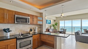 A modern kitchen with stainless steel appliances, wooden cabinets, and a large island. - Encanto Living 1101 -2BR by Kivoya (Puerto Peñasco)