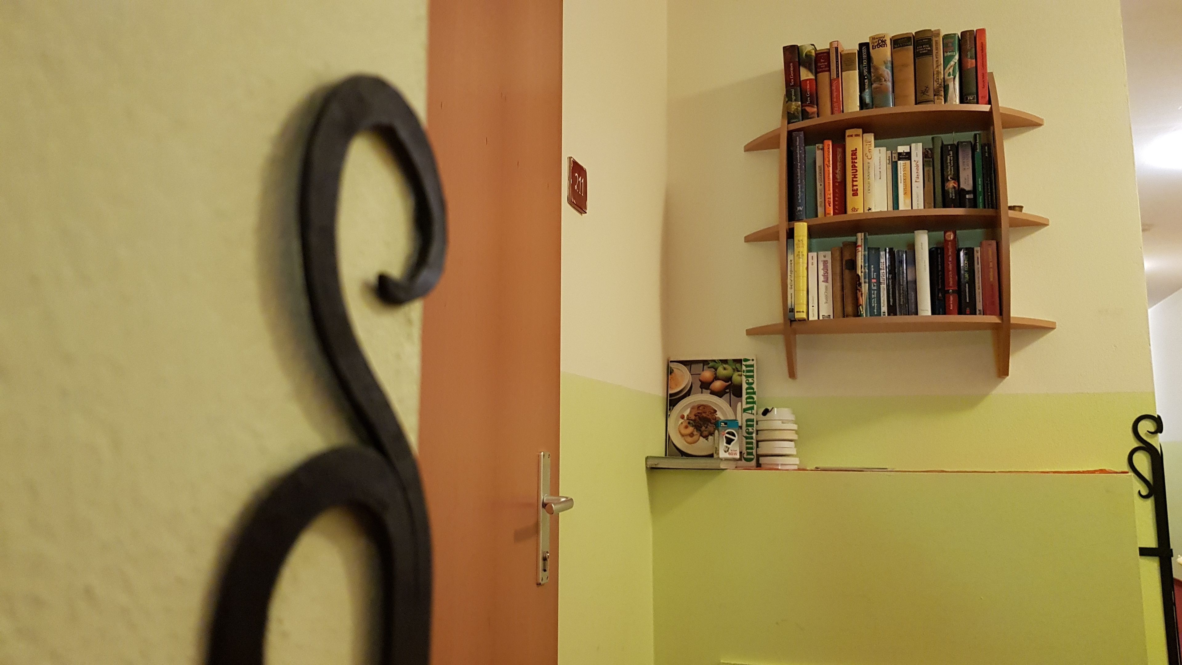 Une pièce avec une bibliothèque remplie de livres, une porte dotée d’une poignée décorative et une plaque numérotée fixée au mur.