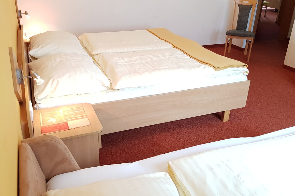 Ein Einzelbett mit Holzrahmen, ein Nachttisch mit Lampe und ein Stuhl in einem Raum mit rotem Teppich.