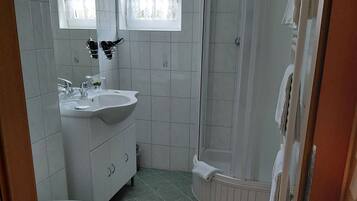Ein Badezimmer mit Toilette, Waschbecken, Spiegel, Fenster, Dusche und Fliesenboden.