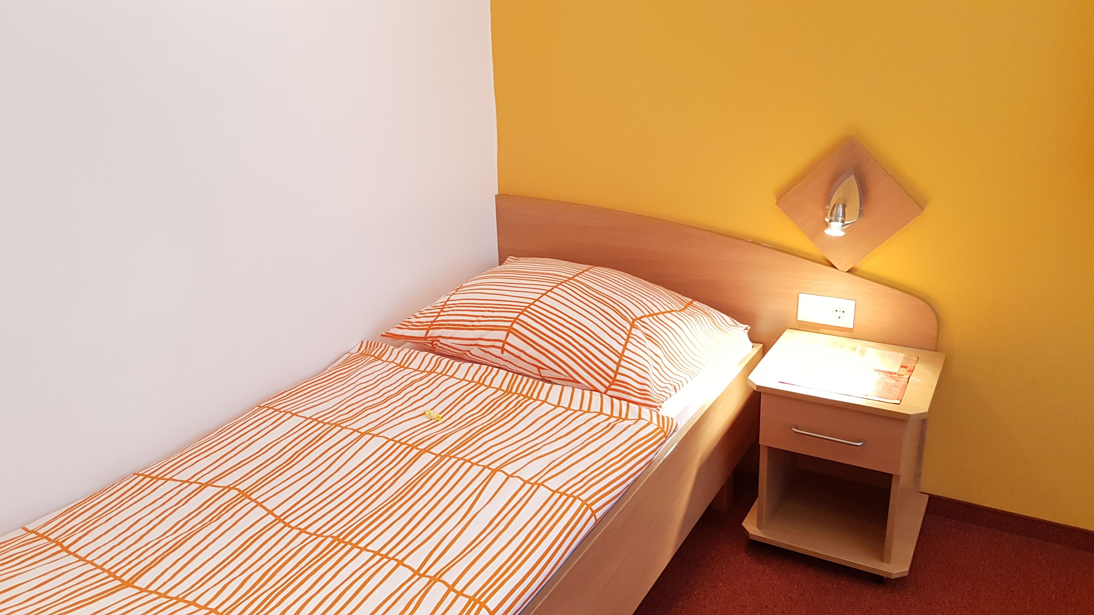 Un lit simple avec une couvre-lit à motifs, une table de chevet avec une lampe et une prise électrique au mur.