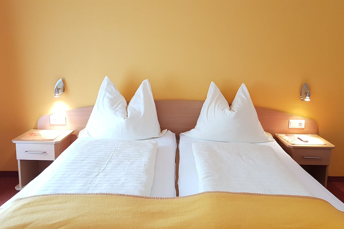A double bed with white linens and a yellow throw blanket, two bedside tables with lamps, and a plain yellow wall.