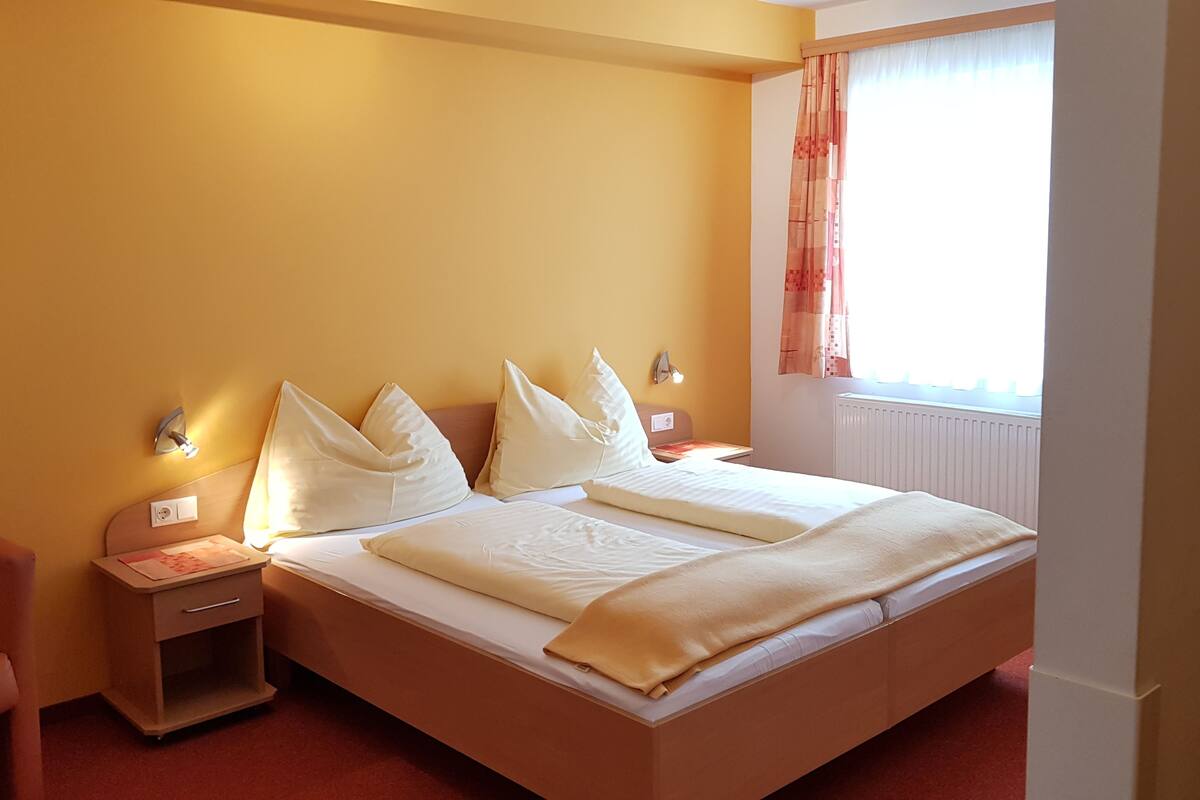 Une chambre d’hôtel avec un grand lit, deux tables de chevet, une petite table et une fenêtre avec des rideaux.