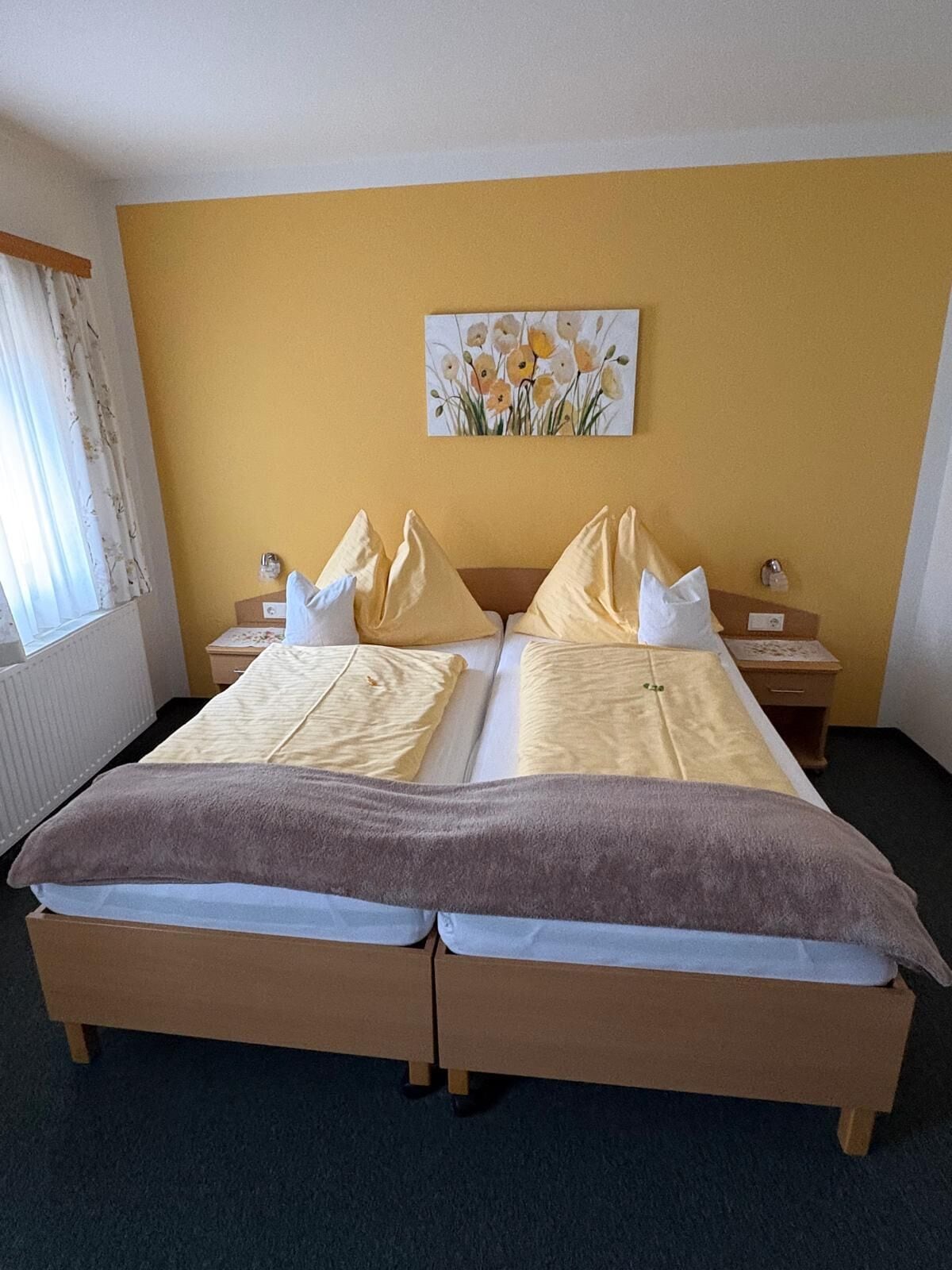 A double bed with a wooden frame, two nightstands, a painting on the wall, and a window with curtains.