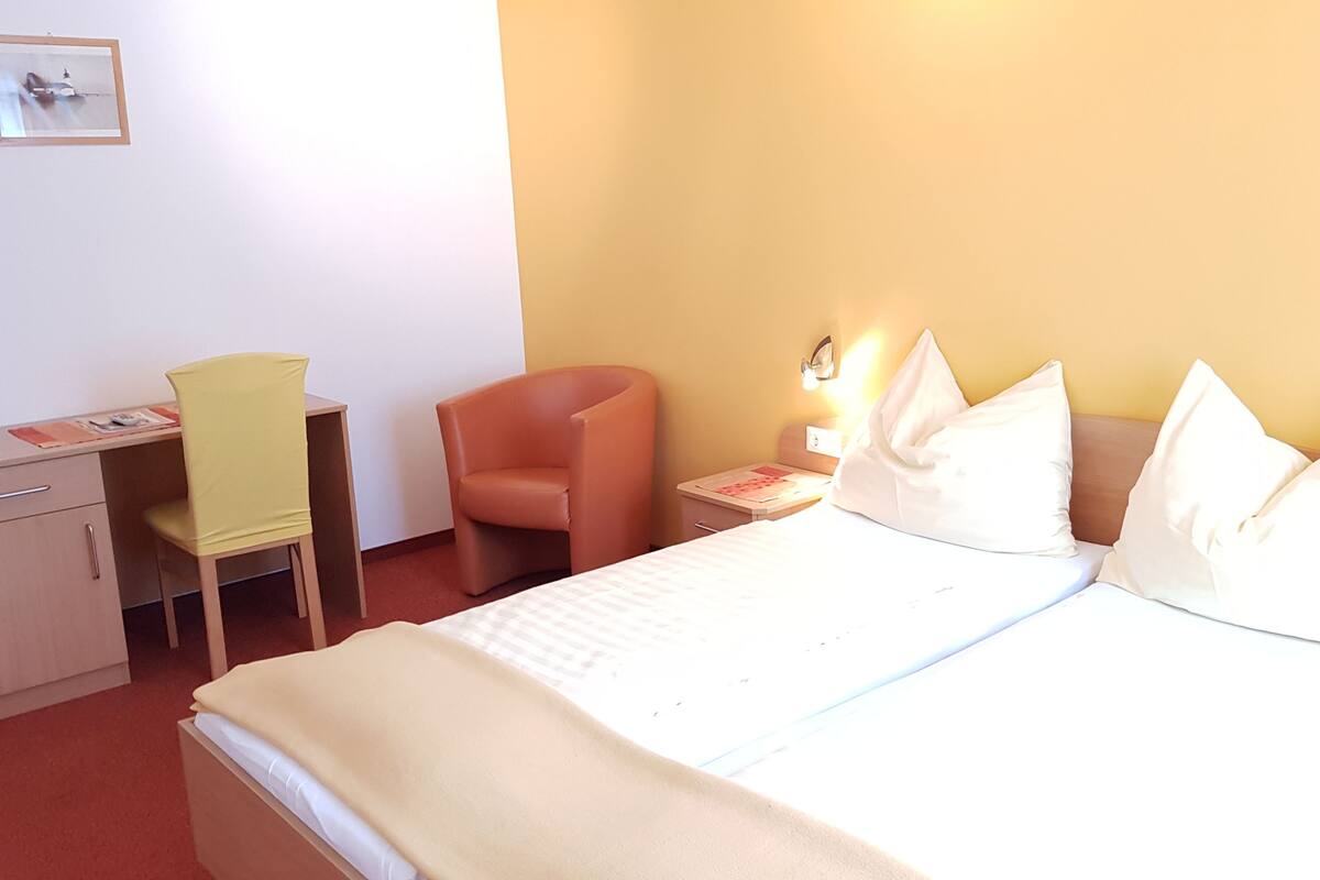Une chambre d’hôtel comprenant un lit, un bureau, une chaise et une table de chevet avec une lampe.
