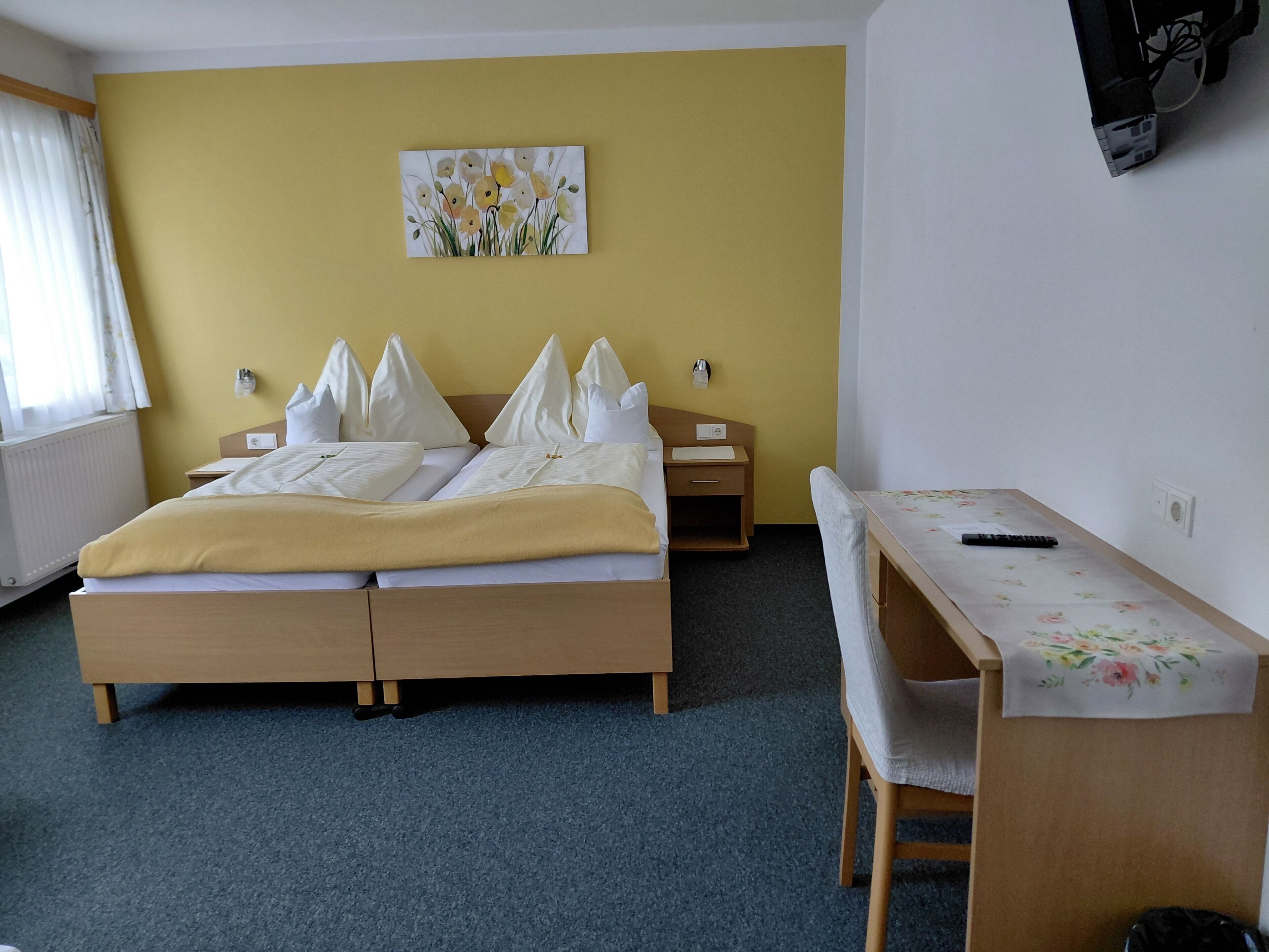 A hotel room with a bed, bedside tables, a desk, and a wall-mounted painting.