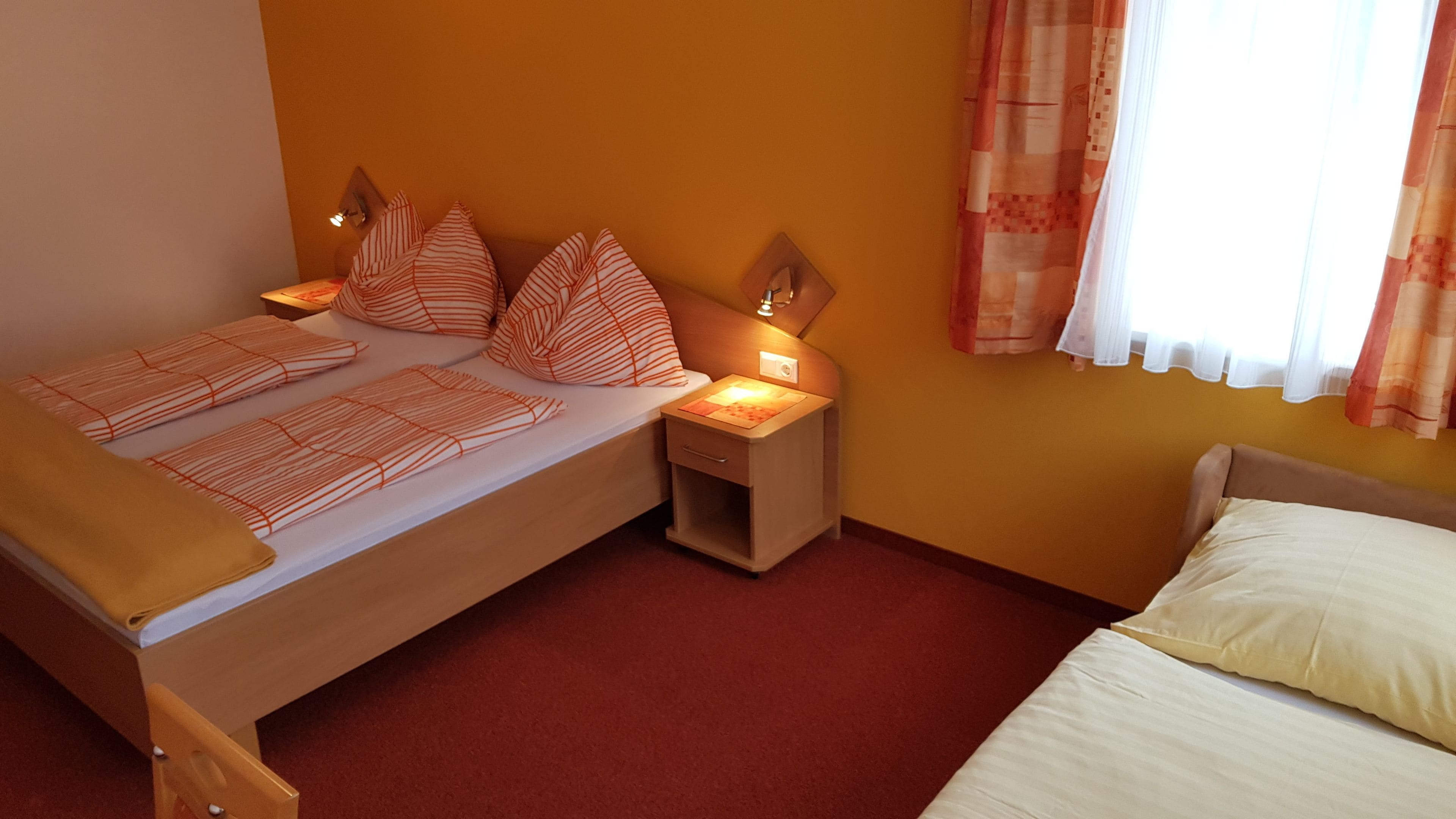 A double bed with striped bedding, a nightstand with a lamp, and a window with curtains.
