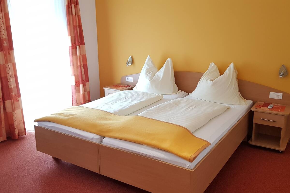 Un lit double avec du linge de lit blanc et un plaid jaune, deux tables de chevet avec des lampes et un luminaire fixé au mur.