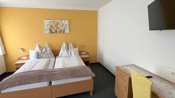 Ein Hotelzimmer mit einem Bett, Nachttischen, einem Schreibtisch, einem Sessel und einem an der Wand befestigten Fernseher.