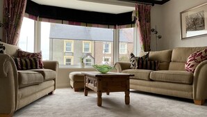 A living room with two beige sofas, a wooden coffee table, and a view of a building through large windows. - Ramsey House (Haverfordwest)